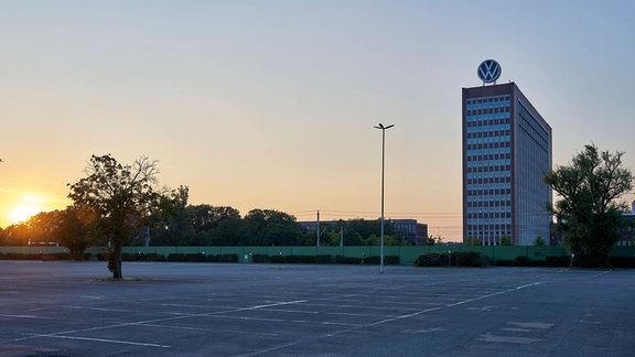 Ein leerer Parkplatz liegt vor einem Gebäude mit VW-Logo auf dem Dach