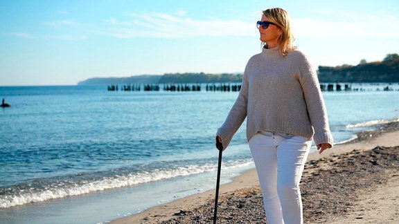 Jana geht am Strand - mit eonem Stock in der rechten Hand.