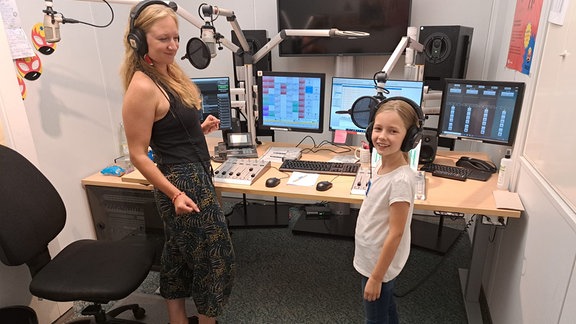 Moderatorin Vivi und Studiogast Selma sitzen nebeneinander im MDR Tweens Studio in Halle. Sie schauen beiden in die Kamera, hinter ihnen sind ein Mischpult, Bildschirme und viele Knöpfe zu erkennen. 