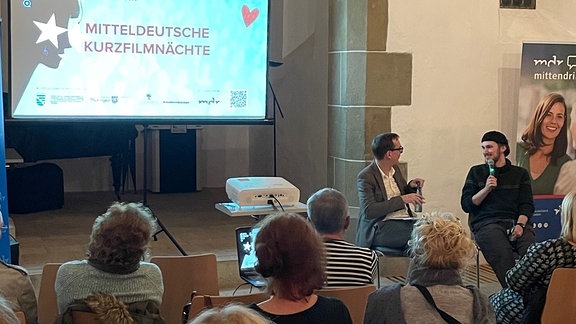 Moderator redet mit Filmemacher vor Publikum