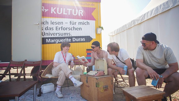 Junge Männer mit Büchern in der Hand vor Bauwagen