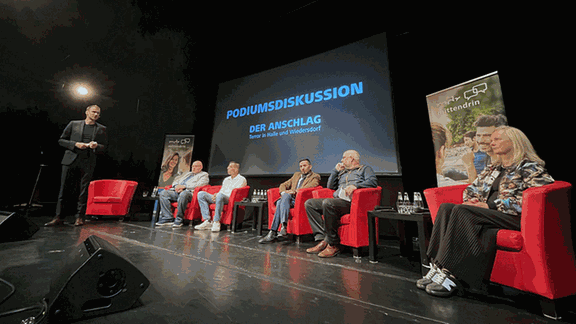 Menschen auf einer Bühne vor großer Leinwand