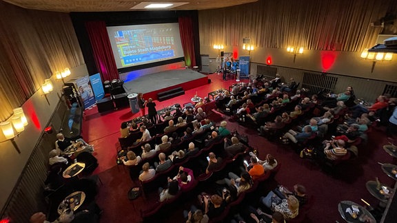 Menschen sitzen in großem Saal vor großer Kinoleinwand