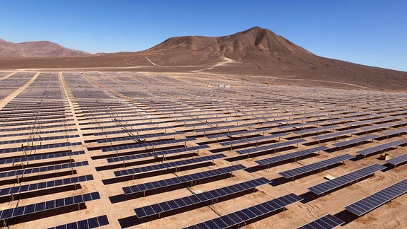 Auf einer weiten, sandigen Fläche stehen viele Solarpanels.