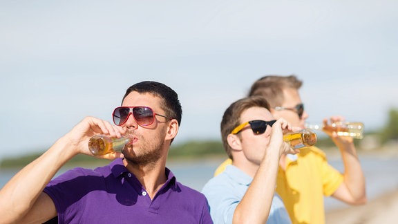 Drei junge Männer trinken aus Flaschen.