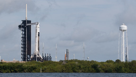 Am Kennedy Space Center in Florida befinden sich zwei Trägerrakten. Im Vordergrund kann man die Falcon-9-Rakete vom privaten Raumfahrtunternehmen SpaceX am Launchpad 39A erkennen. Zu dem Zeitpunkt der Aufnahme wird der Start der Axiom-1-Mission zur ISS vorbereitet. Im Hintergrund befindet sich die Mega-Mondrakete SLS auf dem Launchpad 39B. Nach den abschließenden Tests soll sie die erste Artemis-Mondmission ins All befördern.