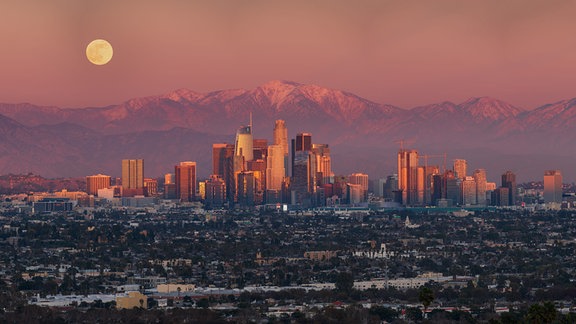 Kategorie: Mensch und Weltall  Mondaufgang über Los Angeles © Sean Goebel  Eine Ausrichtung des Mondes, der Berge und der ikonischen Skyline von Los Angeles nach einem Wintersturm am 18. Dezember 2021.  Aufgenommen mit der Sony ILCE-7M3 Kamera, 324 mm f/8, ISO 200, 1/60 Sekunde Belichtungszeit  Standort: Los Angeles, Kalifornien, USA 