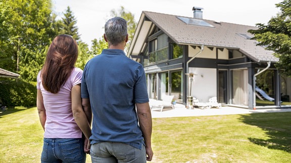 Frau und Mann stehen Hand in Hand vor einem Haus.