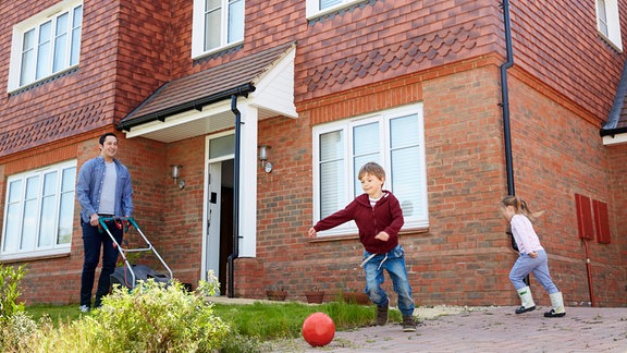 Vater mit zwei spielenden Kindern vor einem Einfamilienhaus