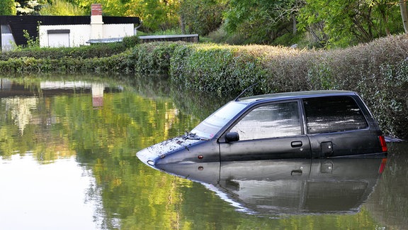 Kleinwagen bis zur Hälfte in Hochwasser versunken in einem Garten, im Hintergrund ein Bungalow