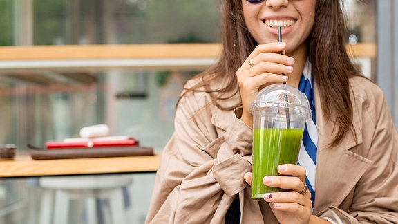 Glückliche Frau trinkt grünen Smoothie.