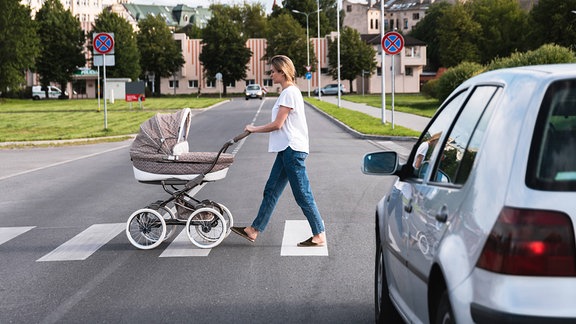 Frau schiebt Kinderwagen über Fußgängerüberweg