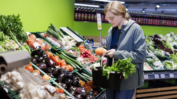 Junge Frau kauft im Supermarkt Gemüse.