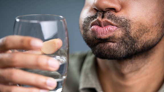 Mann hält Wasserglas und gurgelt.