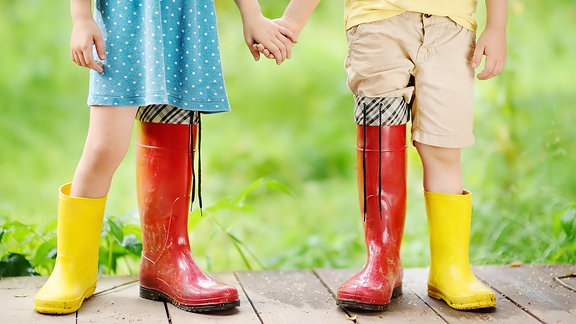 Kinder mit roten und gelben Gummistiefel an den Füßen.