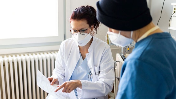 Personen mit Mund- Nasenschutz in einem Krankenzimmer