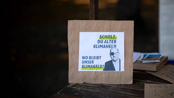 Plakat-Pappe für Demonstration mit Olaf Scholz mit Augenklappe und Spruch Scholz, du alter Klimaheld, wo bleibt unser Klimageld.