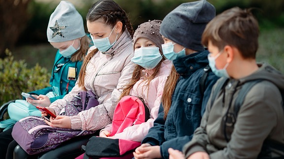 Schulkinder sitzen mit Covidmasken auf einer Bank.