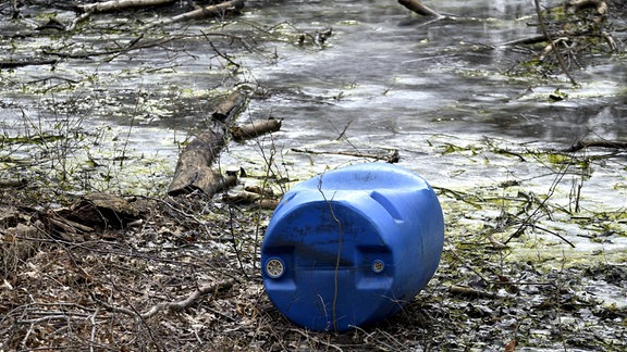 Ein blaues Fass liegt an einem Teich.