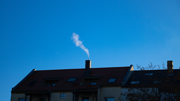 Ein rauchender Schornstein eines Wohngebäudes vor klarem blauen Himmel