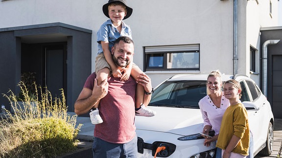 Eine Familie neben einem E-Auto vor einem Einfamilienhaus