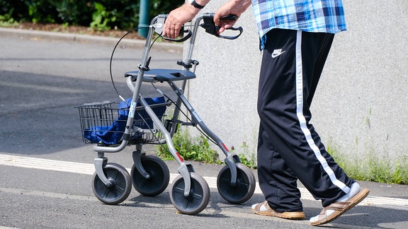 Ein Mann in schwarzer Trainingshose stützt sich beim Gehen auf einen Rollator.