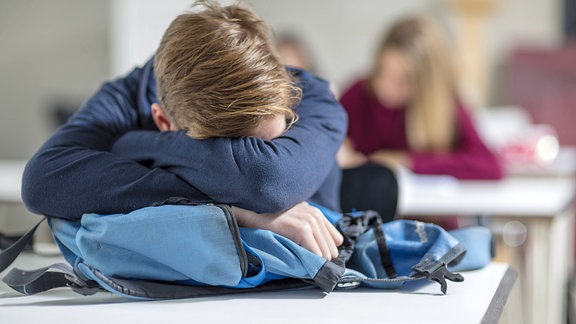 Eine Junge schläft auf einer Schulbank.