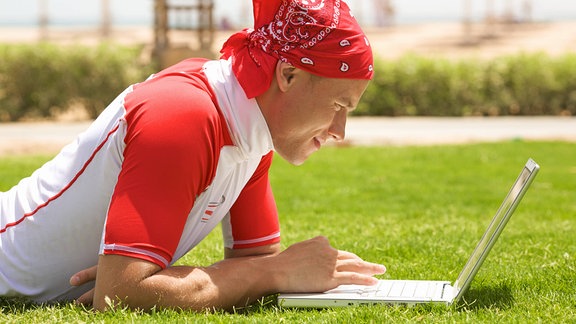 Ein Mann liegt auf einer Wiese und schaut in einen Laptop