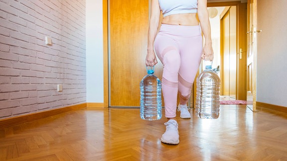 Eine Frau, die Ausfallschritte mit Wasserflaschen macht