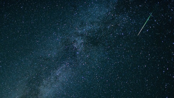 Eine Sternschnuppe leuchtet neben der Milchstraße am Himmel.