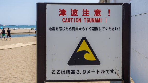 Ein Tsunami-Warnschild steht deutlich im Vordergrund des Bildes.