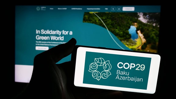 Eine Person hält ein Smartphone mit dem Logo der COP29