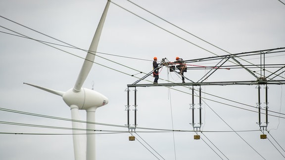 Zwei Personen führen Arbeiten an einem Strommast durch.