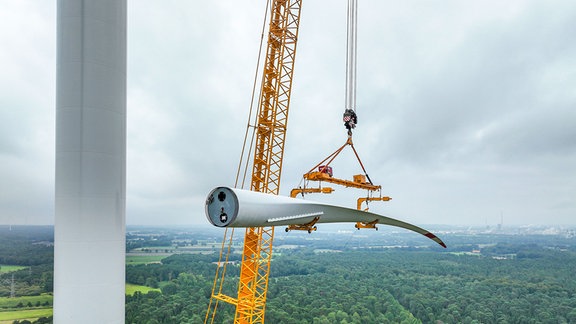 Ein mobiler Grosskran, Autokran, hebt ein Rotorblatt zum Maschinenhaus auf den Turm. 