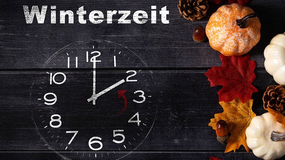 Uhr auf dunklem Holz mit bunten Herbstblättern und Kürbissen