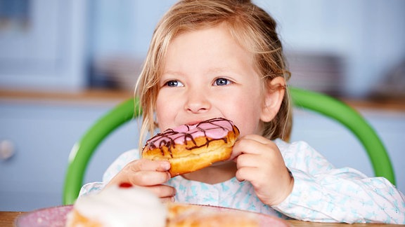 Ein kleines Mädchen beißt herzhaft in einen glasierten Krapfen